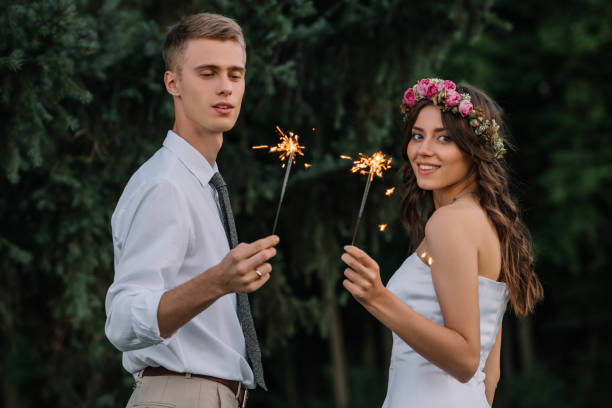 happy young wedding couple holding sparklers and smiling at camera